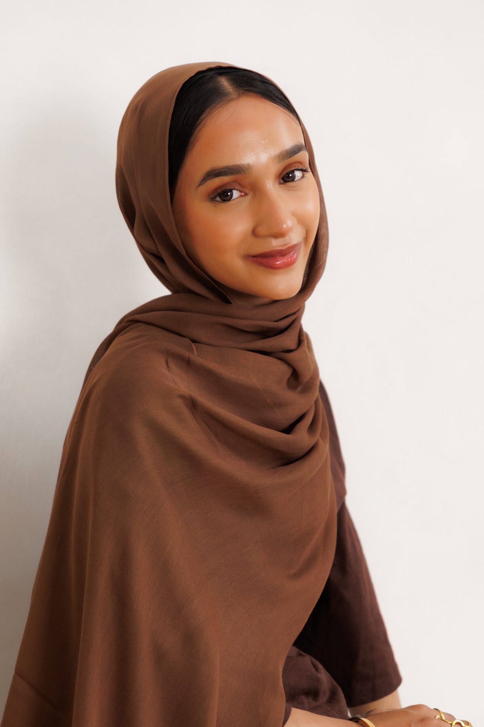 Woman wearing a dark brown hijab with broad draping across the shoulders and upper body