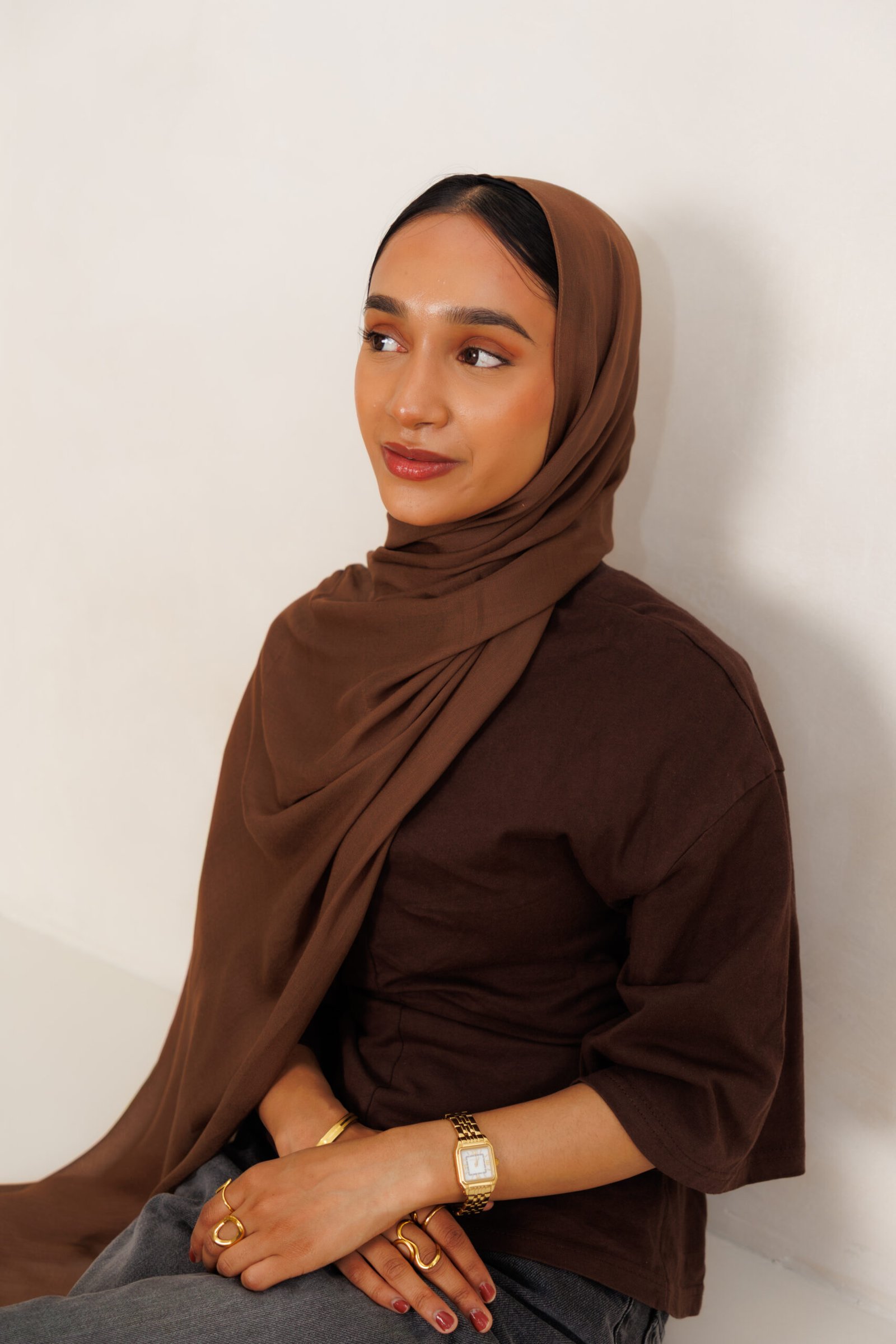Woman wearing a dark brown hijab with layered folds around the face and a long drape across the shoulders